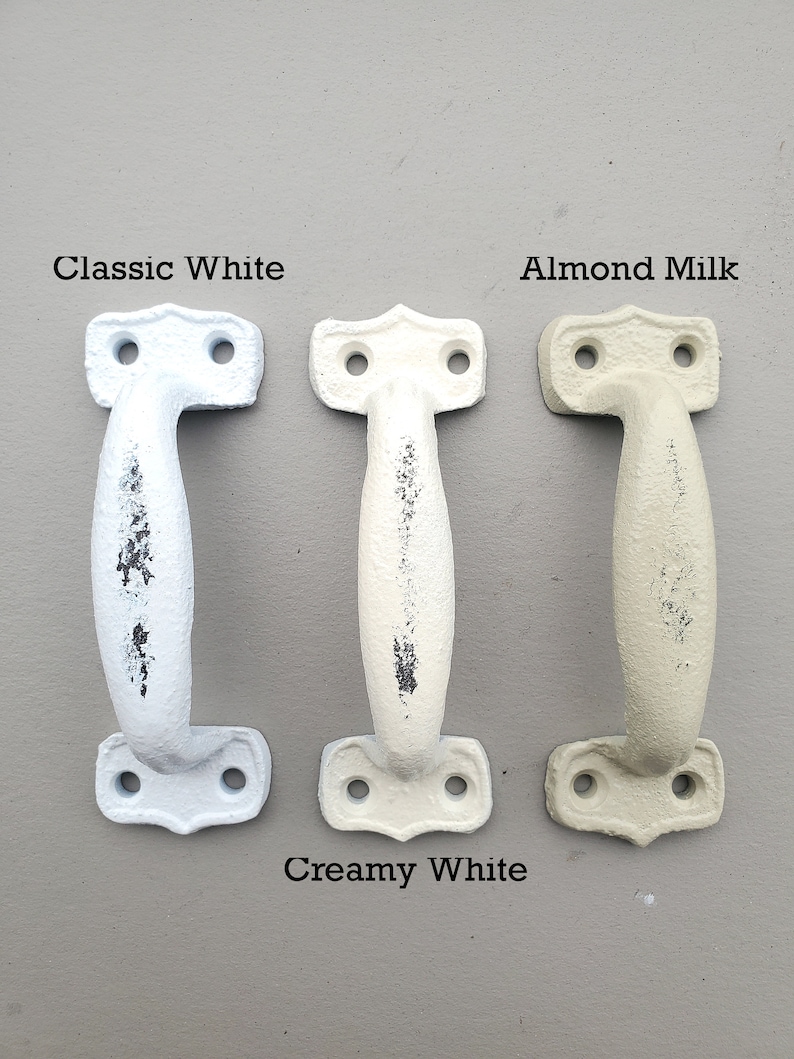 Op de afbeelding: Drie deurgrepen van gietijzer in verschillende tinten wit. De grepen zijn gelabeld met "Classic White", "Creamy White" en "Almond Milk".