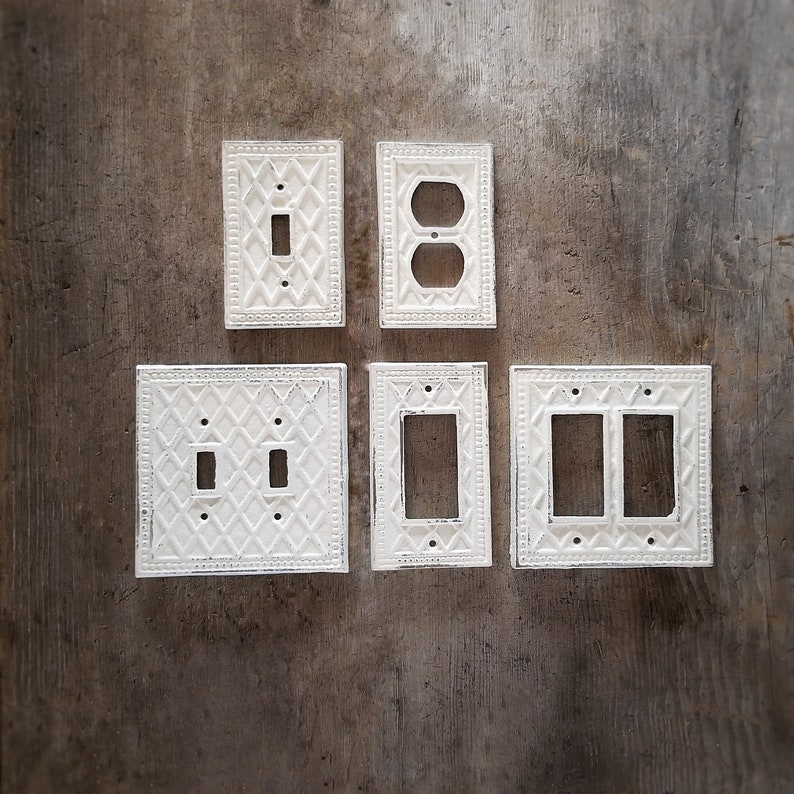 Op de afbeelding: Vijf witte porseleinen lichtschakelaar- en stopcontactbedekkingen met een decoratief ruitpatroon. De afdekkingen zijn in een rij op een bruin houten oppervlak gerangschikt.