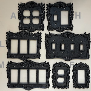 Könnte beinhalten: Satz von acht schwarzen, dekorativen Schalterabdeckungen aus Metall mit verzierten Designs. Die Platten sind für Einzel-, Doppel-, Dreifach- und Vierfachschalter.