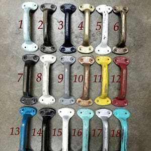May include: Eighteen cast iron drawer pulls in a variety of colours. The pulls are all the same shape, with a rounded top and bottom and a straight handle in the middle. The pulls are arranged in three rows of six, with each row showing a different colour.