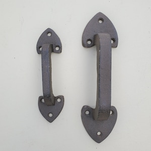 May include: Two black cast iron door handles with a heart-shaped design. The handles are different sizes.