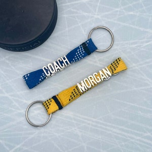 May include: Two hockey keychain lanyards with metal letter charms. One is blue with white accents and says "COACH". The other is yellow with black accents and says "MORGAN".
