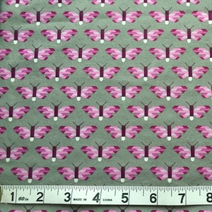 May include: A close-up of a gray fabric with a repeating pattern of pink geometric butterflies. A measuring tape is at the bottom of the image with the numbers 1 through 8 visible.