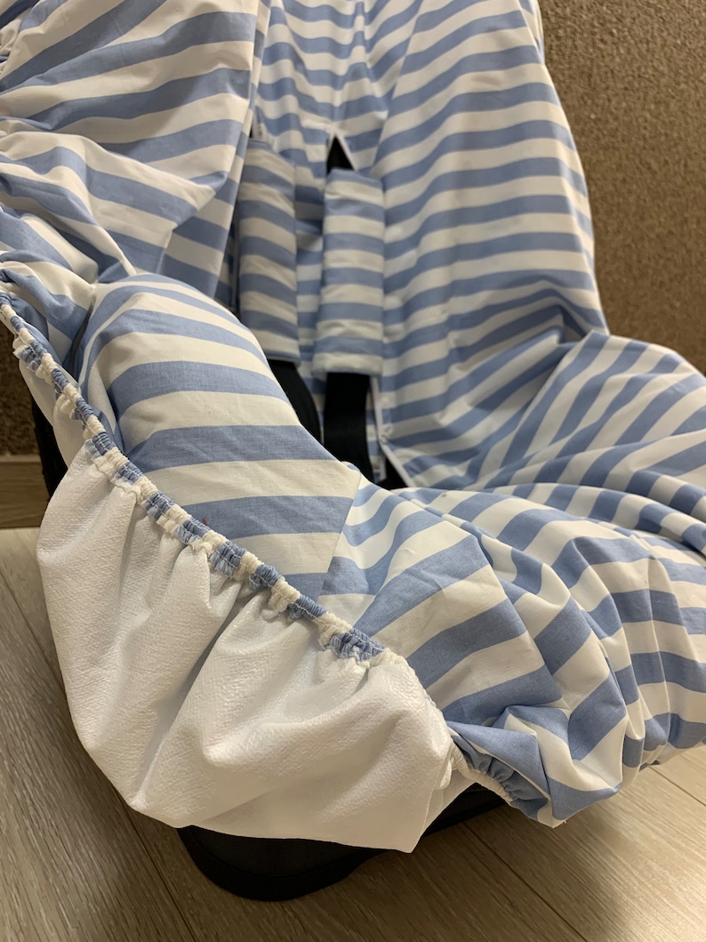 A blue and white striped car seat cover with elastic around the edges. The cover is made of a soft, breathable fabric and is designed to protect your car seat from spills, dirt, and wear and tear.