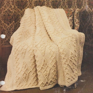 May include: A crocheted throw blanket in a cream color with a diamond pattern. The blanket is draped over a chair with a floral patterned upholstery.