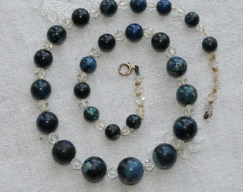 May include: A necklace made of dark blue and clear glass beads. The beads are round and have a mottled appearance. The necklace is strung on a silver chain.
