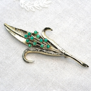 May include: A gold-tone brooch in the shape of a leaf with a cluster of green gemstones.