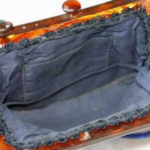 May include: Open view of a vintage handbag with a tortoiseshell frame and a dark blue interior. The frame has a clasp and a beaded handle. The interior is lined with dark blue fabric and has a small pocket.