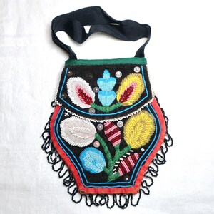 May include: A black beaded bag with a black strap and a green trim. The bag features colourful floral designs in white, yellow, blue, and red. The edges are trimmed with black beads.