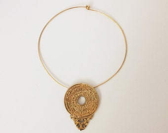 May include: A gold necklace with a circular pendant featuring intricate designs. The pendant has a smaller circle in the center and a decorative bottom.