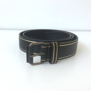 Peut inclure: Une ceinture en cuir noir avec une bordure dorée et une boucle en laiton.