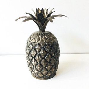 May include: A silver pineapple-shaped container with a textured surface. The container has a lid with a pineapple top.
