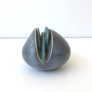 Peut inclure: Une petite sculpture en céramique bleue et verte de forme arrondie. La sculpture présente un design unique avec une série de formes courbes qui se chevauchent.