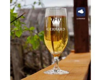 May include: A clear glass beer stein with a white crown and the name "GERHARD" printed on it. The stein is filled with a golden-coloured beer and is sitting on a wooden surface.
