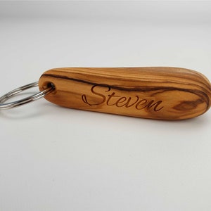 Op de afbeelding: Een houten sleutelhanger met een zilveren ring en de naam "Steven" erop gegraveerd.