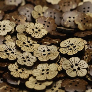 Puede incluir: Una colección de botones marrones con forma de flor hechos de cáscara de coco. Cada botón presenta un diseño de cinco pétalos con cuatro agujeros centrales para coser y líneas grabadas que irradian desde el centro hacia los bordes.