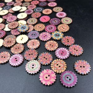 May include: A collection of round wooden buttons with scalloped edges, featuring various colorful printed patterns including floral, geometric, and mandala-like designs. Each button has two central holes for sewing, with some plain cream-colored backs.