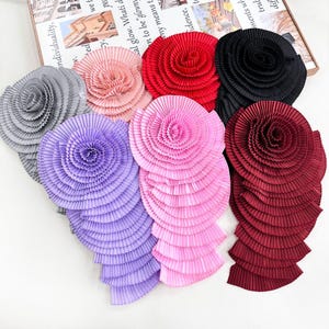 May include: A collection of seven circular fabric rosettes featuring tightly pleated textures. The rosettes are arranged in a cluster and come in various colors including gray, light pink, red, black, lavender, bright pink, and deep burgundy.