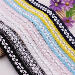 May include: A collection of eight different coloured trims with a ruffled edge and white beads. The trims are black, grey, pink, light blue, white, yellow, navy blue, and light blue.