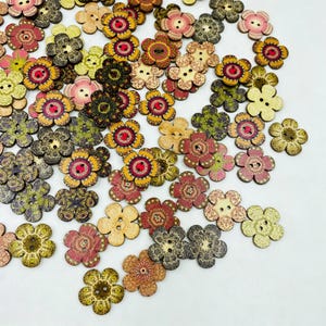 Puede incluir: Una gran colección de botones de madera con forma de flor esparcidos sobre una superficie lisa. Cada botón presenta dos orificios centrales y patrones complejos y multicolores en tonos rojo, amarillo, verde, rosa y marrón con texturas.