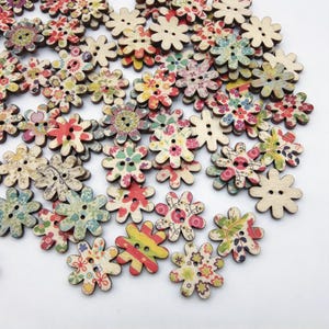 Puede incluir: Una colección de numerosos botones de madera con forma de flor de ocho pétalos redondeados. Cada botón tiene dos agujeros centrales y está decorado con varios patrones florales, geométricos y de rayas de colores, mientras otros son lisos.