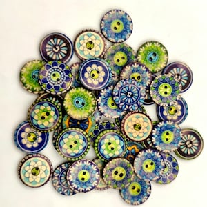 May include: A collection of round wooden buttons featuring various printed patterns in shades of blue, green, and white. Each button has two holes in the center and displays intricate floral or geometric designs across the surface of the wood.