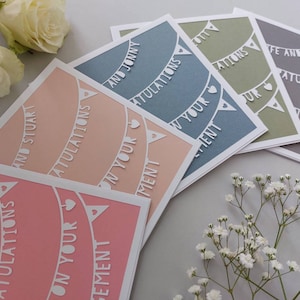 May include: Five cards with a white paper cut-out design of bunting with the words "Congratulations on your engagement" on each card. The cards are in different colors: pink, peach, light blue, green, and gray.
