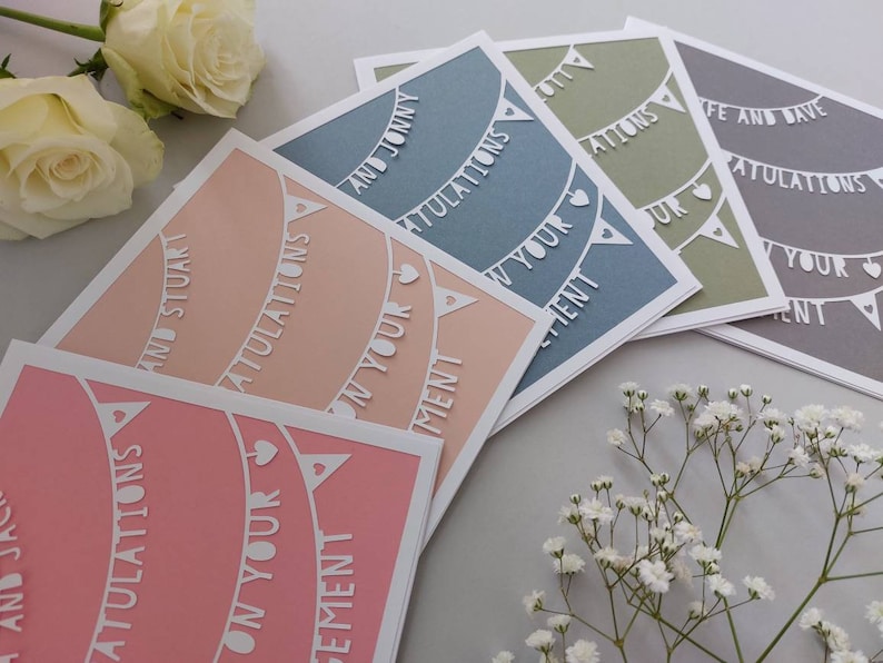 May include: Five cards with a white paper cut-out design of bunting with the words "Congratulations on your engagement" on each card. The cards are in different colors: pink, peach, light blue, green, and gray.