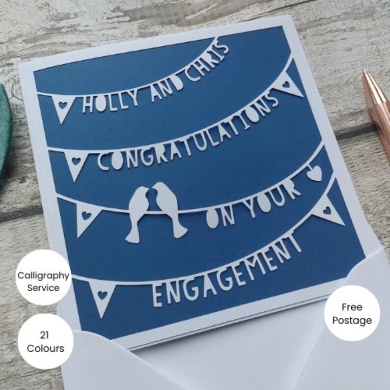 May include: A blue card with white cut-out designs of a banner with the text "Holly and Chris Congratulations on your Engagement" and two birds.