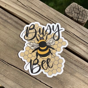 May include: A sticker with a bee on a honeycomb background. The text "Busy Bee" is written in cursive.