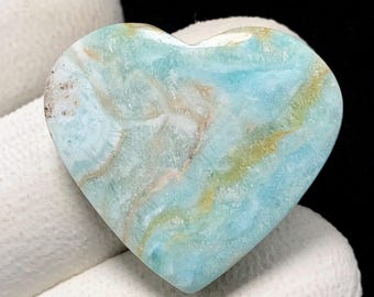 May include: A heart-shaped gemstone, displaying a mix of light blue, white, and golden-brown colours. The polished surface reveals a natural, marbled pattern. Suitable for jewellery making or as a decorative item.