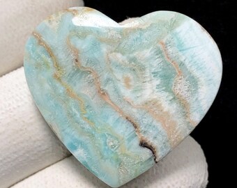 May include: A heart-shaped stone with a polished surface. The stone features a blend of light blue, white, and tan colours, with a marbled appearance. The heart is a decorative item, possibly a paperweight or a collectible.