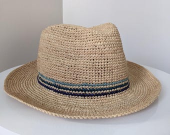 May include: A tan crocheted straw hat with a wide brim and a blue and black striped band around the crown.