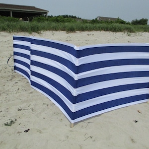 May include: A blue and white striped windbreak for the beach. The windbreak is made of fabric and has a curved shape.