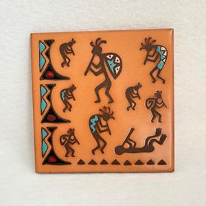 May include: Square, tan-colored tile with a Native American design. The tile features brown figures of Kokopelli playing flutes and carrying shields, with accents of turquoise and black. The design is bordered by triangles.