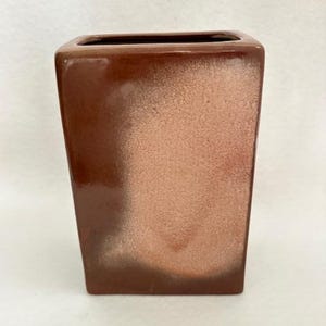 May include: A rectangular ceramic vase with a glossy finish, featuring a deep brown color that transitions into a lighter, textured tan gradient in the center. The vase has a wide, open top and straight vertical sides with rounded corners.