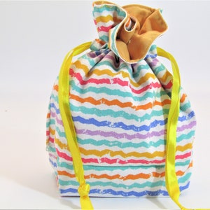 May include: A white drawstring bag with rainbow colored stripes and yellow drawstrings. The bag is made of fabric and has a white background with colorful stripes.