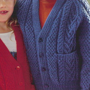 May include: Two children wearing knitted cardigans. The girl is wearing a red cardigan with a button closure and the boy is wearing a blue cardigan with a cable knit pattern.