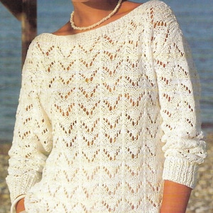 May include: A white crocheted sweater with a delicate openwork pattern. The sweater has a boat neck and long sleeves.