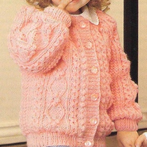 May include: A pink knitted cardigan with a cable knit pattern and button closure. The cardigan has a round neckline and long sleeves.