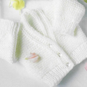Può includere: Un cardigan bianco lavorato a maglia per neonati, con tre bottoni perlati. L'indumento morbido e strutturato è piegato su una superficie bianca, con alcuni petali di fiori sparsi. Il cardigan ha maniche lunghe e scollo a V.
