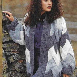 Puede incluir: Una mujer lleva un cárdigan de punto gris, blanco y azul con un patrón geométrico. El cárdigan está abierto por delante y tiene mangas largas. La mujer lleva una camisa azul debajo del cárdigan.