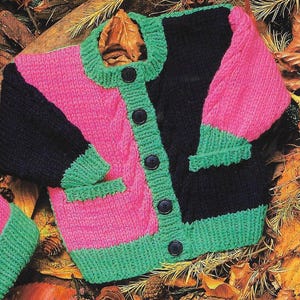 May include: A knitted cardigan with a black, pink, and green color block design. The cardigan has a button closure and a pocket on the front.
