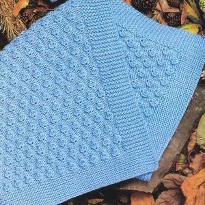 Op de afbeelding: Een lichtblauw gebreid babydekentje met een textuurpatroon. Het dekentje is gemaakt van zacht garen en heeft een delicate, handgemaakte uitstraling.