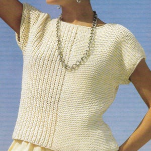 May include: A white knitted top with short sleeves and a scoop neck. The top has a simple design and is made with a fine yarn.