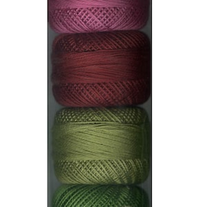 May include: Six spools of embroidery floss in a clear plastic bag. The spools are arranged vertically, with the top spool being pink, followed by a darker pink, then burgundy, then two shades of green, and finally a dark green spool at the bottom.