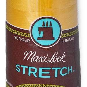 Peut inclure: Une bobine de fil à coudre Maxi-Lock Stretch de couleur or. L'étiquette indique "Maxi-Lock Stretch" et "Soft, Like Yarn Textured Nylon".