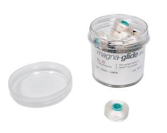 Może przedstawiać: Przezroczysty plastikowy pojemnik wypełniony białymi szpulkami nici. Pojemnik ma etykietę z napisem "magna-glide deluxe" i "No. 40 Trilobal Polyester Col. 10WG1 LINEN".