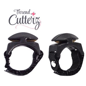 Pode incluir: Dois cortadores de fio dental pretos com tiras ajustáveis. Os cortadores têm uma lâmina de plástico preto e uma lâmina de metal dourado. As tiras são ajustáveis para se adaptarem a diferentes tamanhos de dedos.