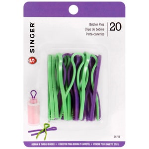 May include: A package of 20 green and purple bobbin pins for sewing. The package says "Bobbin Pins, Clips de bobina, Porte-canettes" and "20".